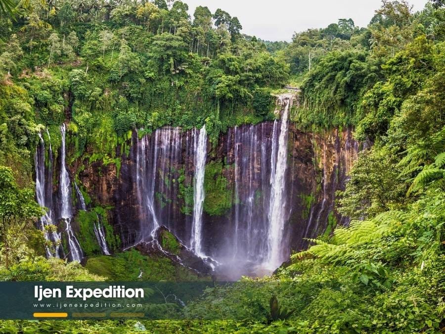 Traveler trekking through the wet canyon floor at the base of Tumpak Sewu Waterfall
