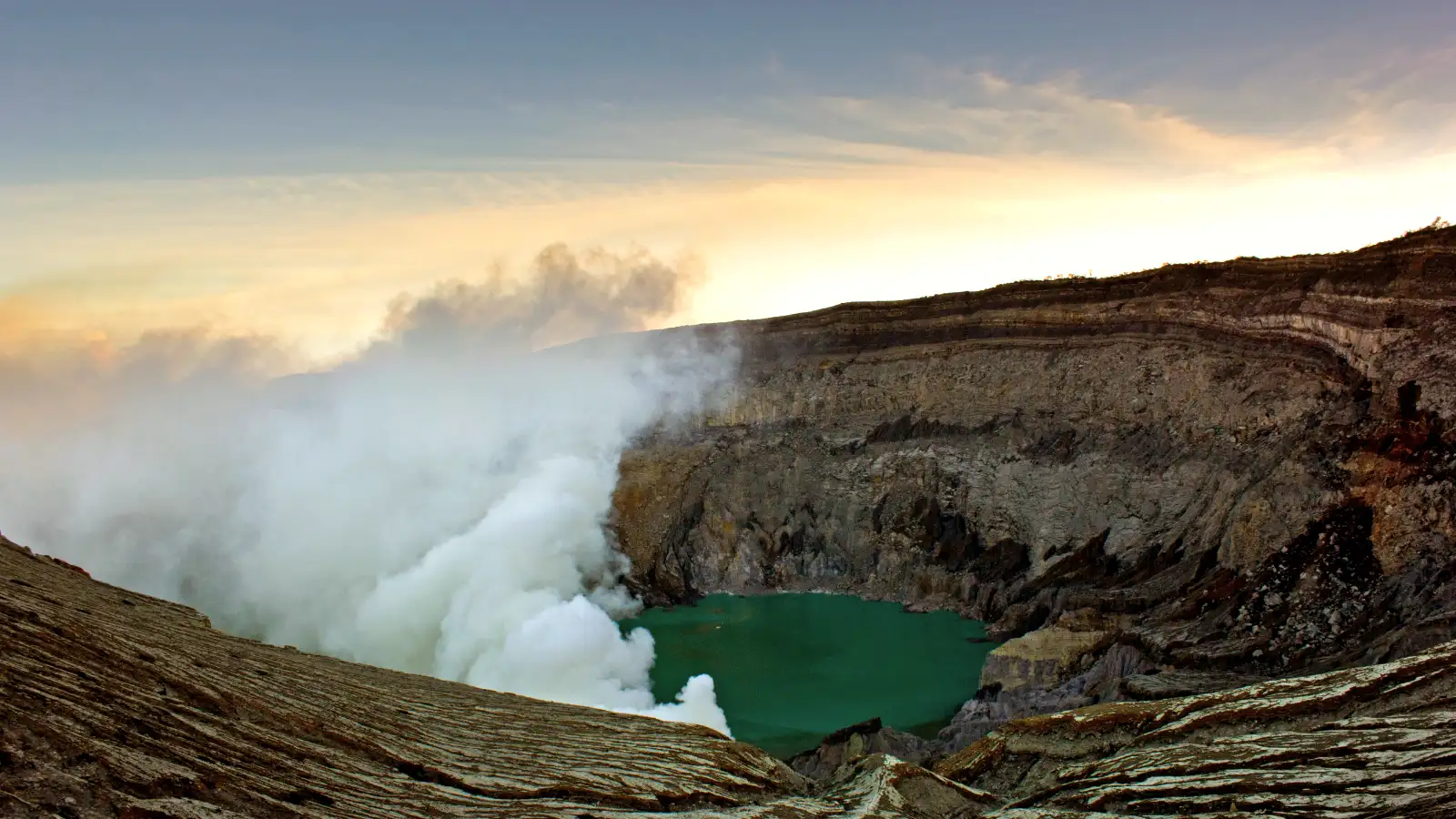 Hikers walking along the narrow ridge of Ijen Crater with sulfuric smoke in the background