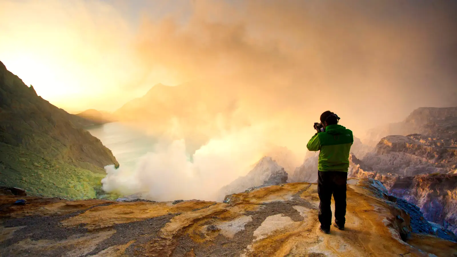 Group of hikers celebrating at the summit of Mount Ijen with the crater lake in the background