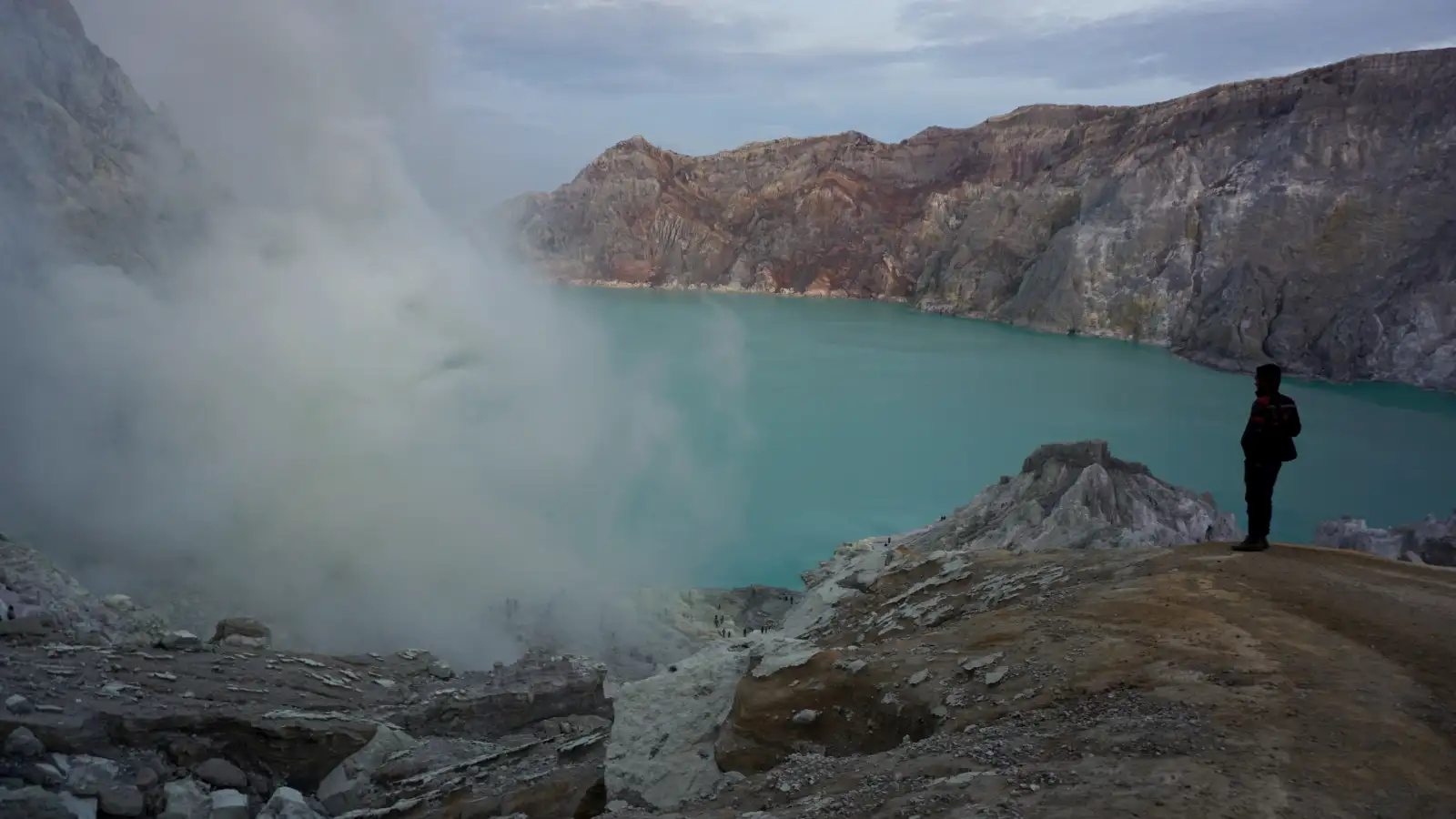 Golden sunrise glow hitting the volcanic rim of Ijen Crater with sulfur smoke in the distance