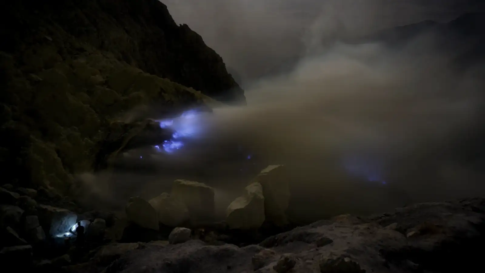 Sulfur Miners and Volcanic Gas Sulfur miners working amidst the thick smoke and blue flames inside Ijen Crater