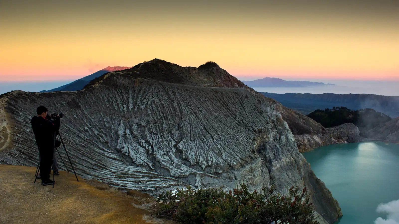 Backpacker wearing a gas mask standing on the rim of Ijen crater at sunrise