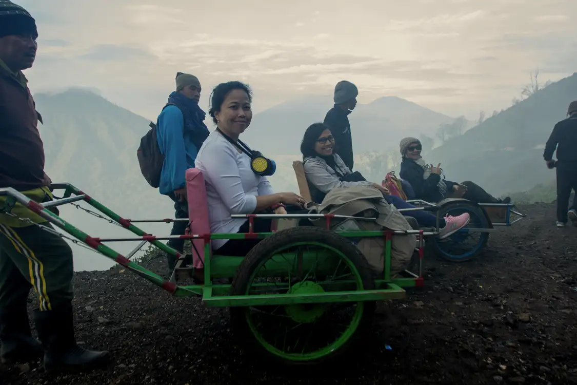 Sulfur miners pushing a passenger trolley up the steep slopes of Ijen Crater during a night trek